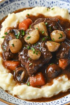 a blue and white plate topped with mashed potatoes and beef