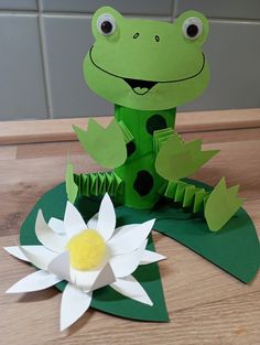 a paper frog sitting on top of a table next to a flower