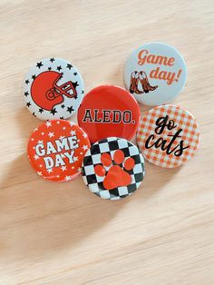 six sports themed buttons sitting on top of a wooden table with the words game day printed on them