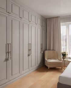 a bedroom with white cabinets and a beige chair in front of a window that looks out onto the city