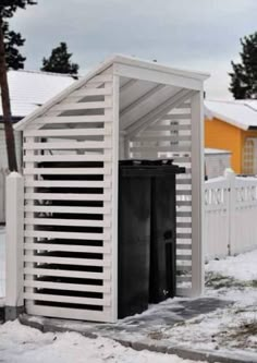 two black trash cans sitting in the snow next to a white fence and yellow house