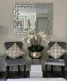 two chairs and a vase with flowers in it sitting on a rug next to a mirror