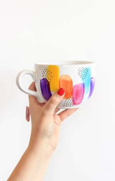 a person holding a coffee cup with colorful paint on it