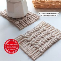 two knitted coasters sitting on top of a table next to a white cup