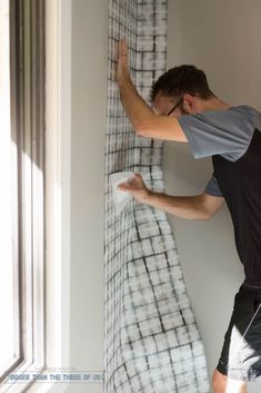 a man is painting the wall in his bedroom with white and black plaid fabric on it