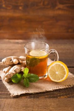 a cup of hot tea with lemon and ginger on a wooden table next to some fresh mint