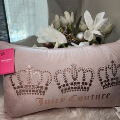 a pink pillow with a crown on it next to some white flowers and a window