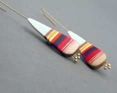 two pairs of earrings with wooden beads hanging from hooks on a gray surface, one is white and the other is red