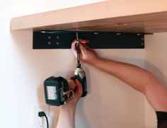 a person using a drill to fix a shelf