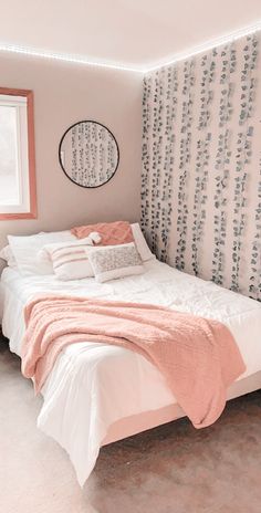 a white bed sitting under a window next to a wall mounted clock on a wall