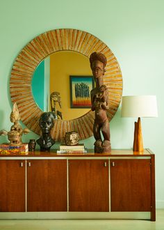 a table with a mirror and some statues on it in front of a wall mounted sculpture