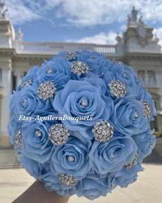 a bridal bouquet with blue roses and crystal brooches in front of a building