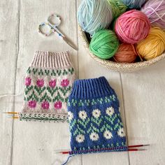 two knitted mittens next to a basket of balls of yarn and knitting needles