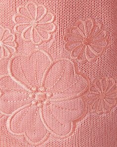 an embroidered pink sweater with white flowers on the front and back, close up view