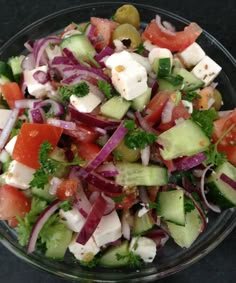 a salad with tomatoes, cucumbers, onions and feta cheese in a glass bowl