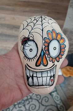 a hand holding a painted rock in the shape of a skull with flowers on it