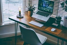 an open laptop computer sitting on top of a wooden desk next to a white chair