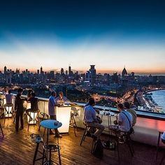 people are sitting at tables on top of a building overlooking the water and cityscape