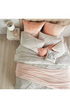 a bed with pink and grey pillows on top of it next to a night stand