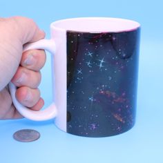 a hand holding a coffee mug with stars on it and a coin in front of it