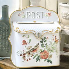 a white mailbox with flowers and birds painted on it's front, sitting on a shelf