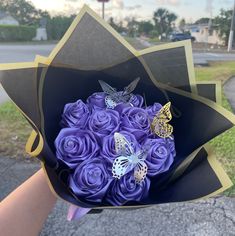 a person holding a bouquet of purple roses with butterflies on them in their hand,