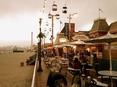 people are sitting at tables on the boardwalk next to the water and buildings in the background