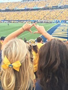 two girls making the v sign with their hands at a football game in front of a large crowd