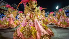 a group of women dressed in pink and gold dance on the street at an event