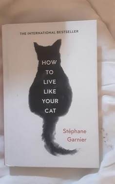 the book how to live like your cat by stephanie garnier is laying on a bed