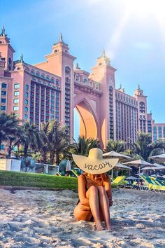 a woman sitting on the beach in front of a hotel with a cowboy hat over her head