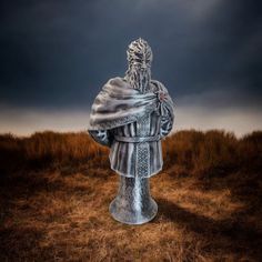 a statue in the middle of a field with dark clouds above it and grass on the ground