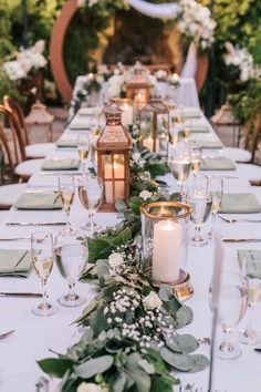 a long table is set with candles and greenery for an outdoor wedding reception in the garden