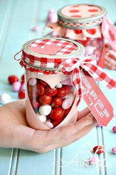 a hand holding a jar filled with red and white candies on top of a table