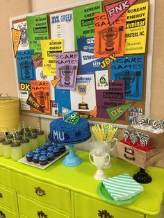 a green table topped with cake and cupcakes next to a wall covered in posters