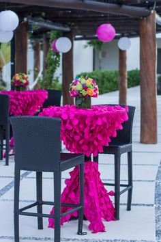 an outdoor dining area with black chairs and pink table cloths, lanterns and flowers