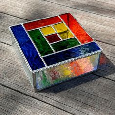 a multicolored glass box sitting on top of a wooden table next to a piece of wood