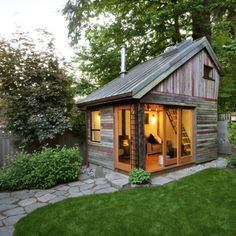 a small wooden shed sitting on top of a lush green field next to a forest