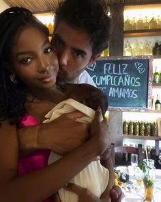 a man holding a baby in his arms while standing next to a woman at a bar