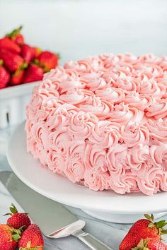 a cake with pink frosting and strawberries on the side, next to two plates of strawberries