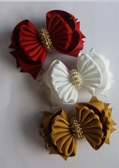 three different colored hair bows on a white surface with gold and red beads in the center