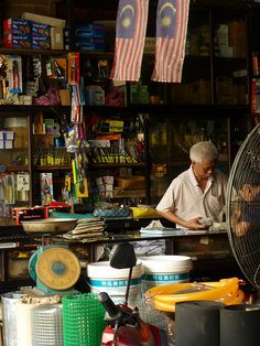 a man working in a store with many items on the shelves and around him is a fan