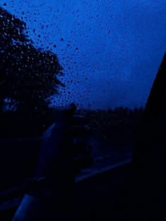 a person holding an umbrella in the rain at night with trees and blue sky behind them