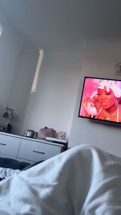 a flat screen tv mounted on the wall above a bed with white sheets and pillows