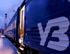 a blue train traveling down tracks next to a loading platform