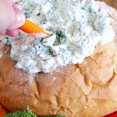 a person dipping something into a bread bowl with broccoli on the side and carrots