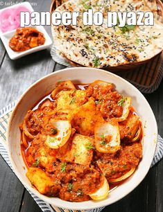 two bowls filled with food on top of a wooden table next to a plate of naan bread