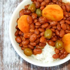 a white bowl filled with beans and rice on top of a wooden table next to a fork