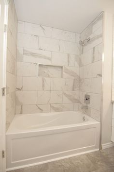 a white bathroom with marble tile walls and bathtub in the corner, along with toilet paper on the wall