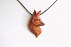 a wood carving of a dog's head hanging from a leather cord on a white wall